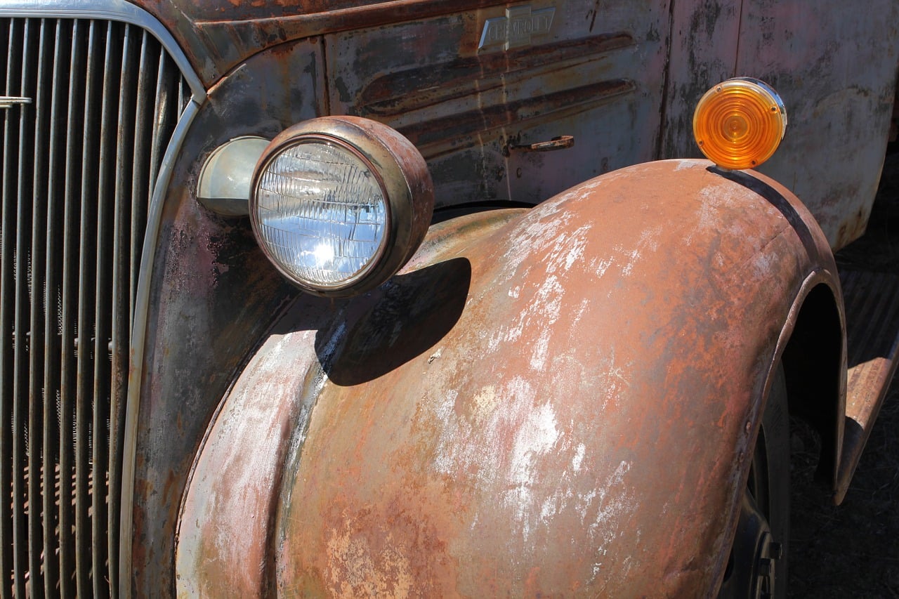 Close-up of the rusty front fender, headlight, grille, and turn signal on an antique Chevrolet truck.